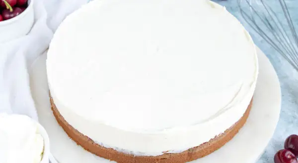 Ein runder Kuchen mit einer dicken Schicht luftiger **Mascarponecreme**. Kirschen und ein Schneebesen deuten auf die Zubereitung hin.