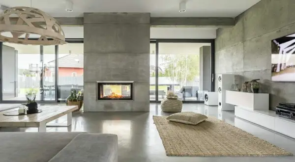 Nowoczesny salon z kominkiem obłożonym betonem architektonicznym. Podłoga i ściany również wykonane z mikrobetonu, tworząc spójną, minimalistyczną przestrzeń.