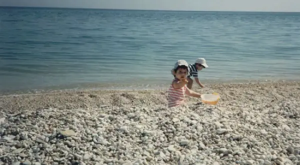 Bambini giocano sulla spiaggia di ciottoli a Marina di Montemarciano, con il mare azzurro sullo sfondo.