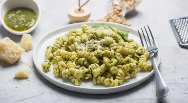 Fusilli z aromatycznym makaronem z pesto ze słoika, posypane parmezanem. Obok miseczka z sosem, kawałki sera i orzeszki piniowe.