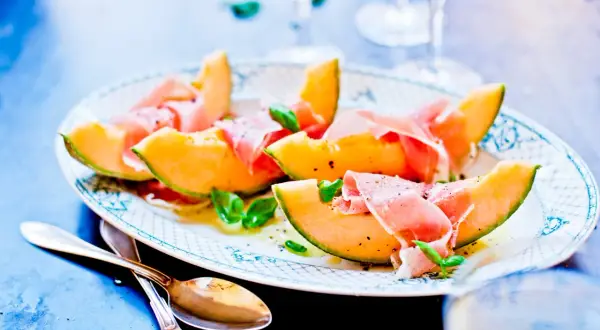 En vacker tallrik med melon och skinka, garnerad med basilika och peppar. Perfekt för en lätt och elegant förrätt.