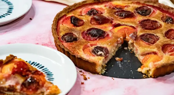 Une délicieuse tarte aux prunes rouges, garnie de poudre d'amande, est prête à être dégustée. Une part a déjà été servie.