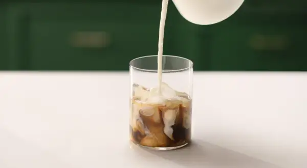 Mjölk hälls i ett glas med is och kaffe. Perfekt för ett enkelt iskaffe recept.