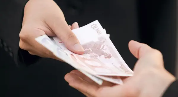 Dwie dłonie przekazują sobie banknoty euro. Zastanawiasz się, ile kosztuje windykacja należności?