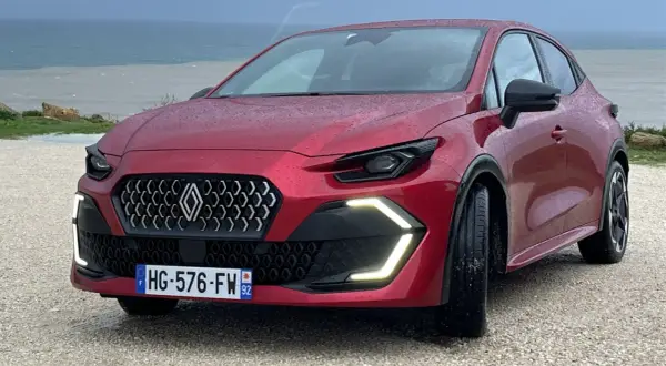 Nowe Clio 2026 w kolorze czerwonym, z nowoczesnym grillem i światłami LED, zaparkowane nad morzem.