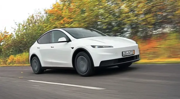Biały Tesla Y w ruchu, otoczony rozmazanymi jesiennymi drzewami. Czy warto kupić?