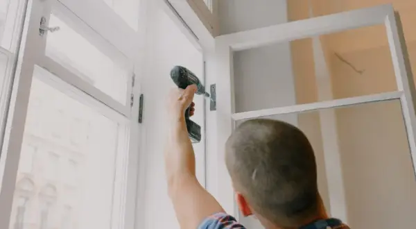 Mężczyzna przykręca zawias w oknie. Szybka wymiana okna to klucz do komfortu.