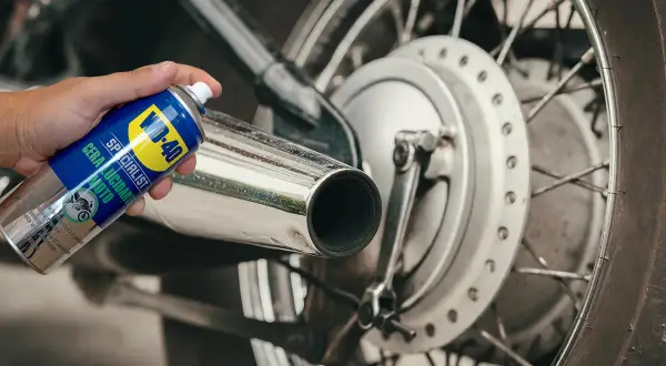 Mano che spruzza cera lucidante WD-40 su uno scarico cromato per lucidare la moto.