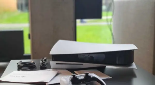 Konsola PlayStation 5 z kontrolerem i kablami na czarnym stole.