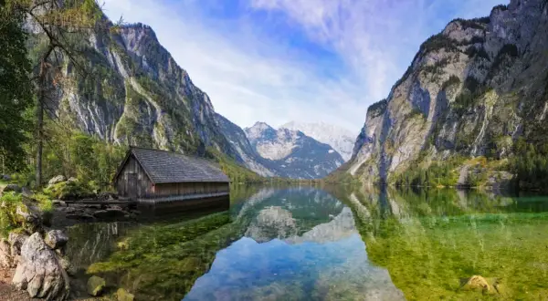 Holzhütte am Königssee, ein Juwel in Bayern, spiegelt sich im klaren Wasser vor majestätischen Bergen.