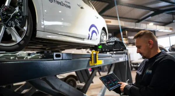 Mechaniker prüft mit Tablet die Achsvermessung an einem Auto. Die Spur verstellt, wird hier präzise eingestellt.