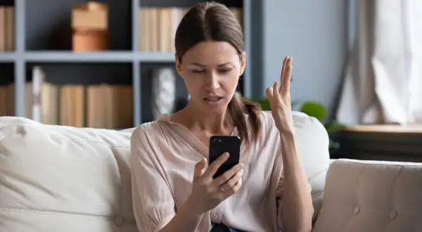 Zirytowana kobieta sprawdza telefon, który nie ma internetu.