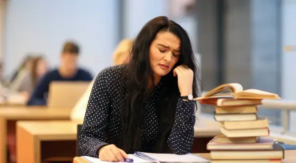 Verzweifelte Studentin mit Büchern. Sie überlegt, ob sie das **uni wechseln** soll.