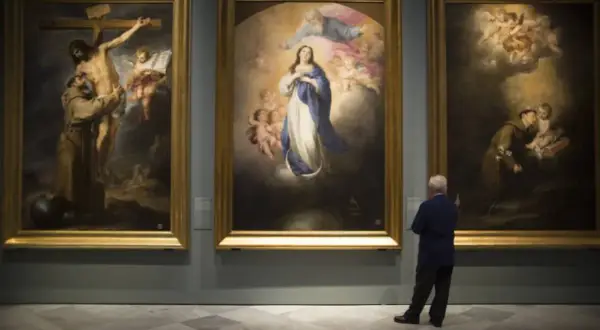 A man contemplates three religious paintings by Bartolomé Esteban Murillo in a gallery.