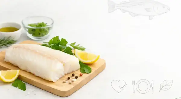 Świeży filet z dorsza na desce z cytryną i ziołami. Niska zawartość dorsz kcal czyni go idealnym wyborem dla dbających o linię.