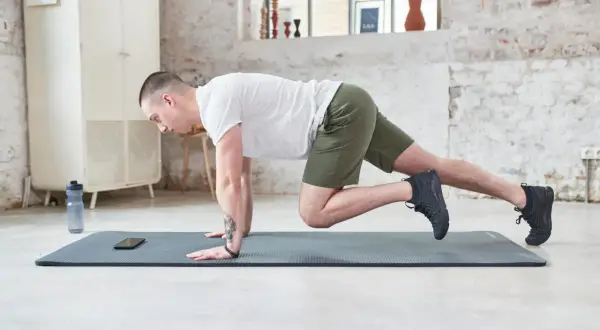 Un homme en short vert effectue un exercice de gainage latéral sur un tapis de yoga.