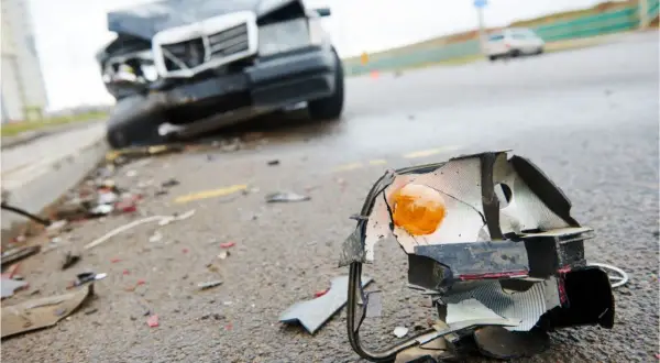 Rozbity reflektor leży na drodze obok zniszczonego samochodu. To dowód na to, że nawet drobna kolizja może przerodzić się w poważny wypadek.