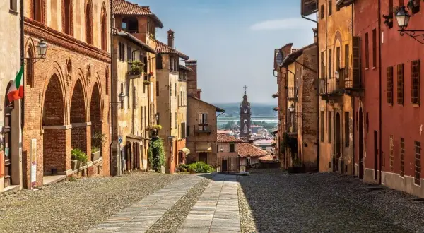 Rue pavée bordée de maisons colorées, avec une église au loin. Un charmant village du Piémont, Italie.