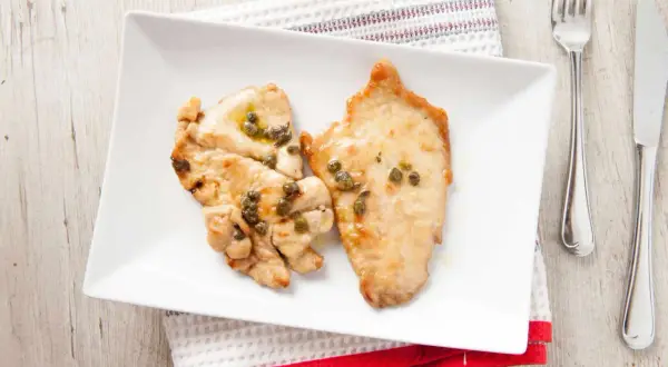 Due fette di fesa di tacchino con capperi su un piatto bianco. Un pasto leggero, ideale per chi cerca fesa di tacchino calorie.