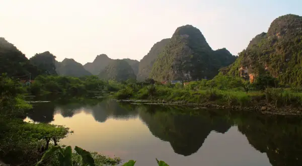 Krajobraz Ninh Binh z odbijającymi się w wodzie wapiennymi górami porośniętymi zielenią.