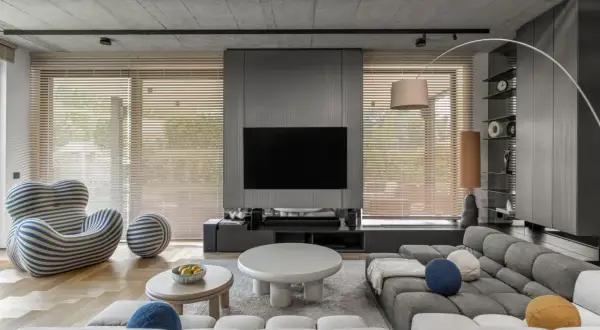 Nowoczesne, minimalistyczne wnętrza z szarą sofą, designerskim fotelem i betonowym sufitem.