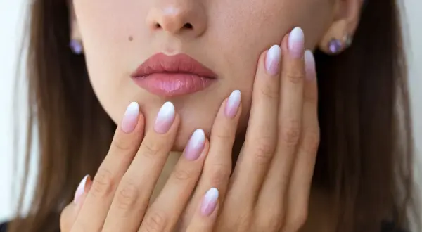 Delikatne baby boomer nails na dłoniach kobiety, z subtelnym ombre od różu do bieli.