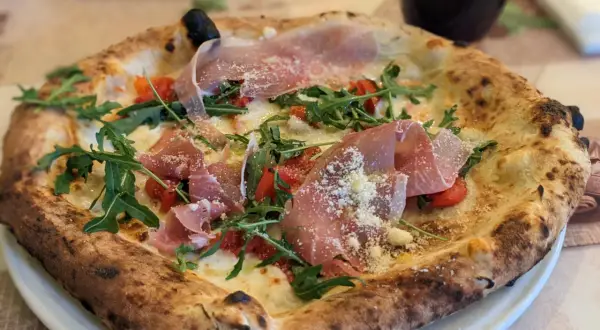 Eine köstliche Pizza mit Prosciutto, Rucola und Tomaten, die aussieht wie die beste Pizza Neapels.
