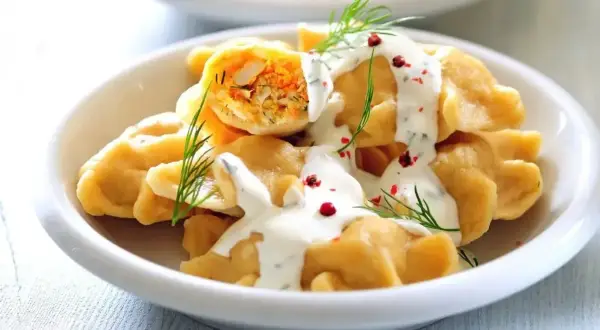 Pierogi z farszem, polane sosem, udekorowane koperkiem i pieprzem.