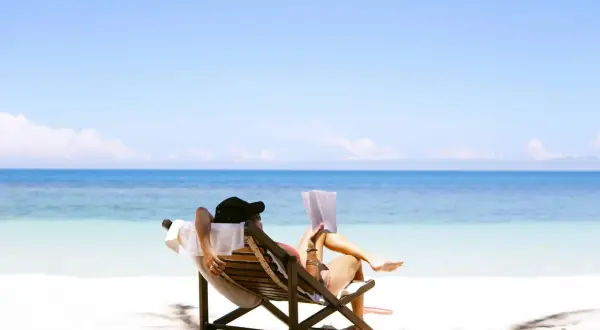 Relaks na plaży z książką – idealne miejsce na wakacje. Błękitne morze i biały piasek tworzą rajski krajobraz.