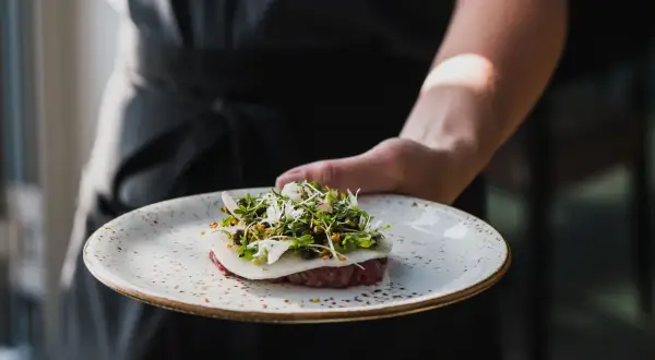 En kock presenterar en vacker tartar med örter och blommor, en delikatess från Torekov Hotell meny.