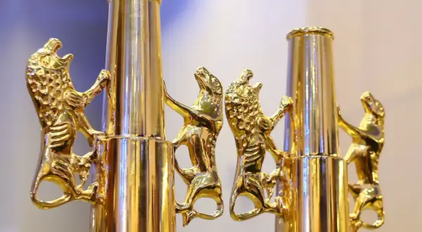 Złote lwy wspinają się po błyszczących, cylindrycznych elementach, tworząc elegancką dekorację.