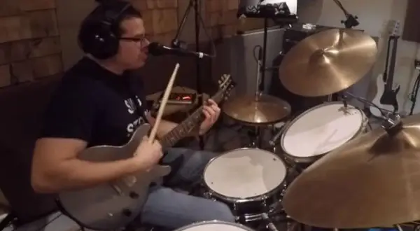 Muzyk w słuchawkach gra na gitarze i perkusji, jakby wpadł w **rush tom sawyer**.