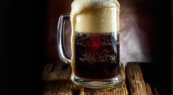 Boccale di birra scura con schiuma abbondante, forse la birra americana più famosa, su un tavolo di legno rustico.