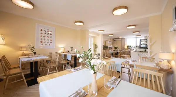 Przytulna restauracja z drewnianymi stołami i krzesłami, idealna na urodziny w łodzi dla dorosłych. Jasne ściany, subtelne oświetlenie i świeże kwiaty tworzą miłą atmosferę.