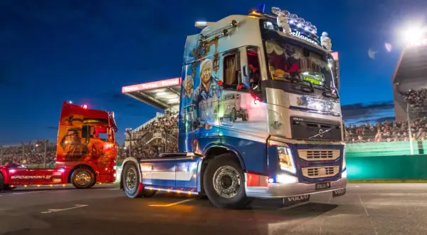 Deux camions décorés, dont un aux couleurs de Spiderman, défilent sur la piste du Mans devant une foule en délire.