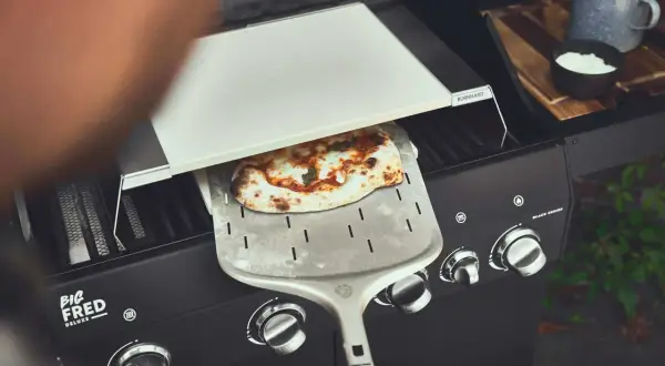 Frisch gebackene Pizza auf dem Pizzaschieber, bereit für den Gasgrill.