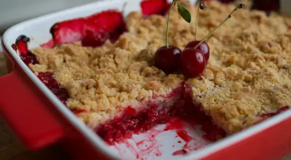 Un délicieux crumble fruits rouges, garni de cerises fraîches, sort du four.