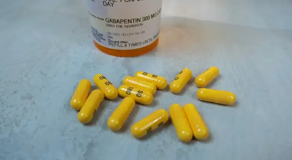 Żółte kapsułki leku Gabapentin 300 mg rozsypane obok butelki z lekiem.