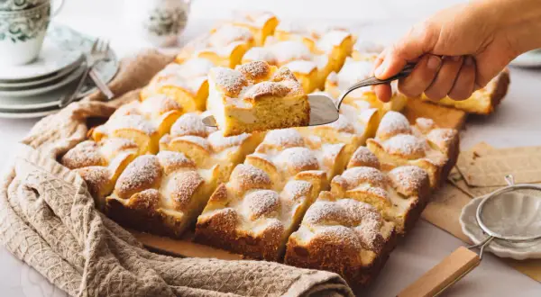 Ein frisch gebackener Ploatz, mit Puderzucker bestäubt, wird aus der Form gehoben. Ein köstliches Rezept für süße Momente.