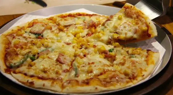 Pyszna hawajska pizza z ananasem, szynką i kukurydzą, właśnie podana.