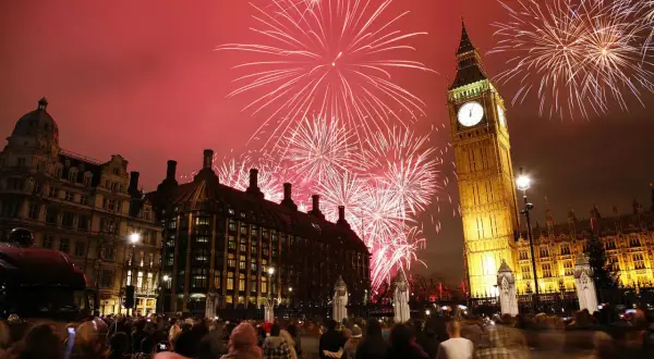 Fuegos artificiales iluminan el cielo sobre el Big Ben y el Parlamento, celebrando las festividades inglesas con una multitud expectante.