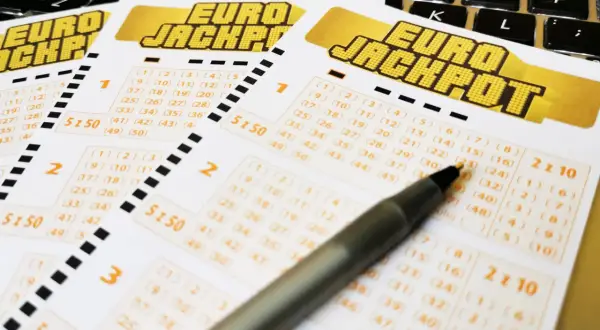 Kupony Eurojackpot leżące na klawiaturze, z długopisem wskazującym na liczby.