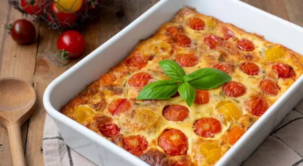 Un délicieux clafoutis tomates cerises, doré et garni de basilic frais, prêt à être dégusté.