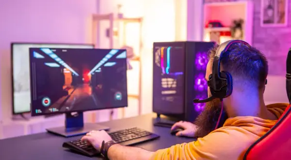 Gamer mit Headset spielt am PC. Die leuchtende Grafik auf dem Monitor und der beleuchtete PC-Tower deuten auf die Vorteile eines Twitch Partners hin.