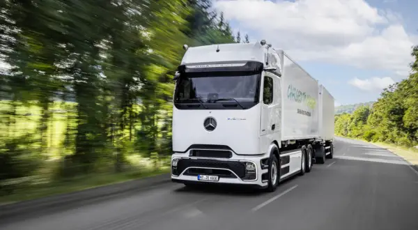 Un camion électrique Mercedes eActros GigaSpace roule sur une route bordée d'arbres.