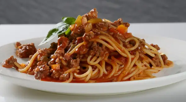 Ein Teller Spaghetti Bolognese, liebevoll zubereitet, mit frischem Basilikum garniert. Perfekt, um bolognese selber machen zu lernen.