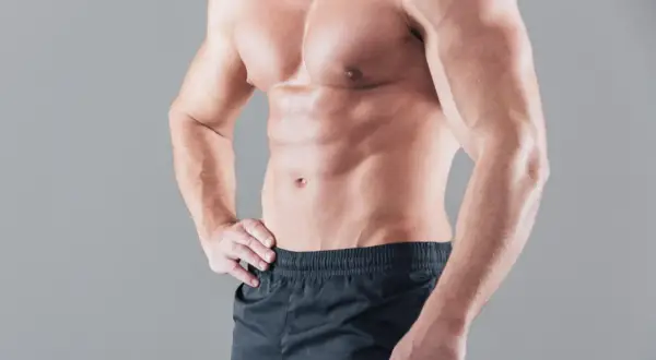 Ein naturaler Bodybuilder mit definierten Bauchmuskeln und Armen steht im Profil.