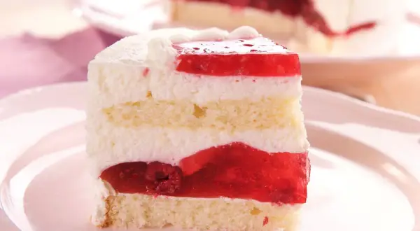 Ein saftiges Stück Frau Holle Kuchen mit Biskuit, Sahne und roter Fruchtschicht.