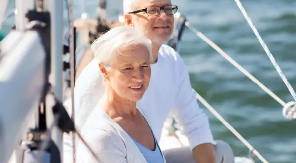 Uśmiechnięta para seniorów na żaglówce. Idealne wczasy świąteczne dla samotnych seniorów, by poczuli się jak na romantycznym rejsie.