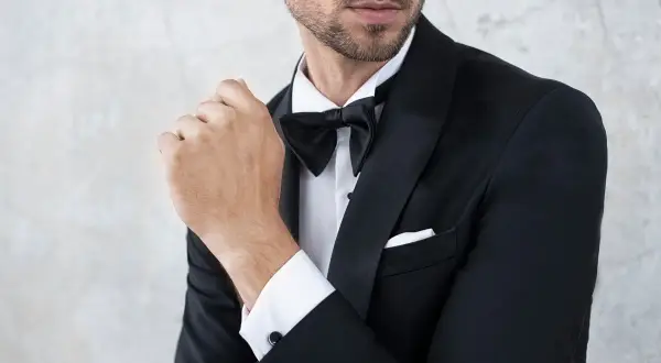 Elegancki mężczyzna w smokingu, z zapiętą muchą. Pokazane detale stroju, jak zapiąć muchę.